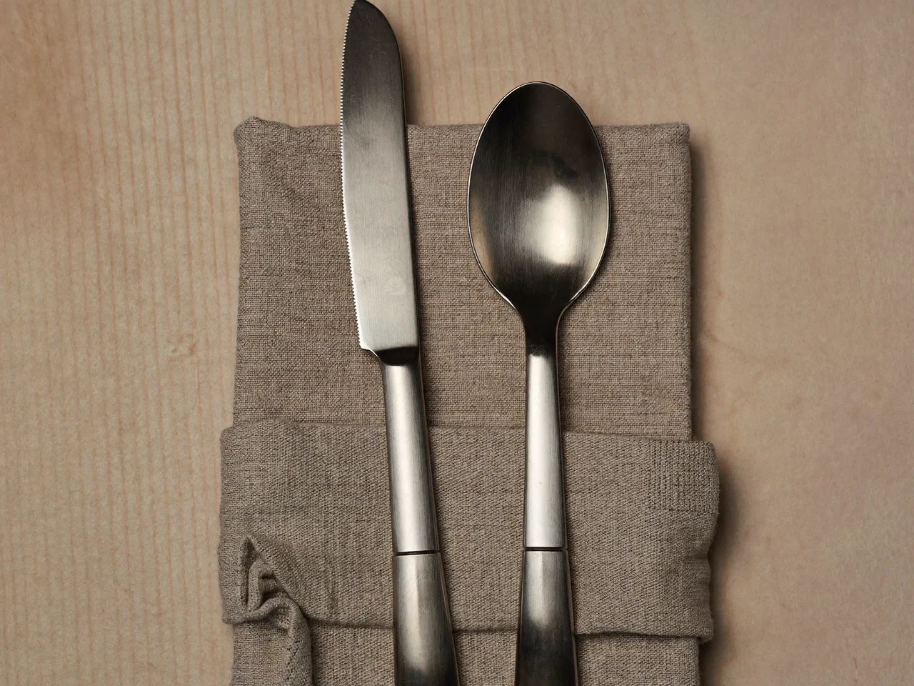 Mat børstet bestik med kniv, gaffel og ske på foldet naturligt linned