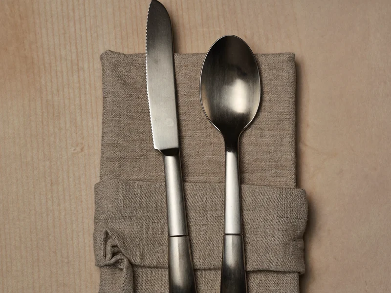 Mat børstet bestik med kniv, gaffel og ske på foldet naturligt linned