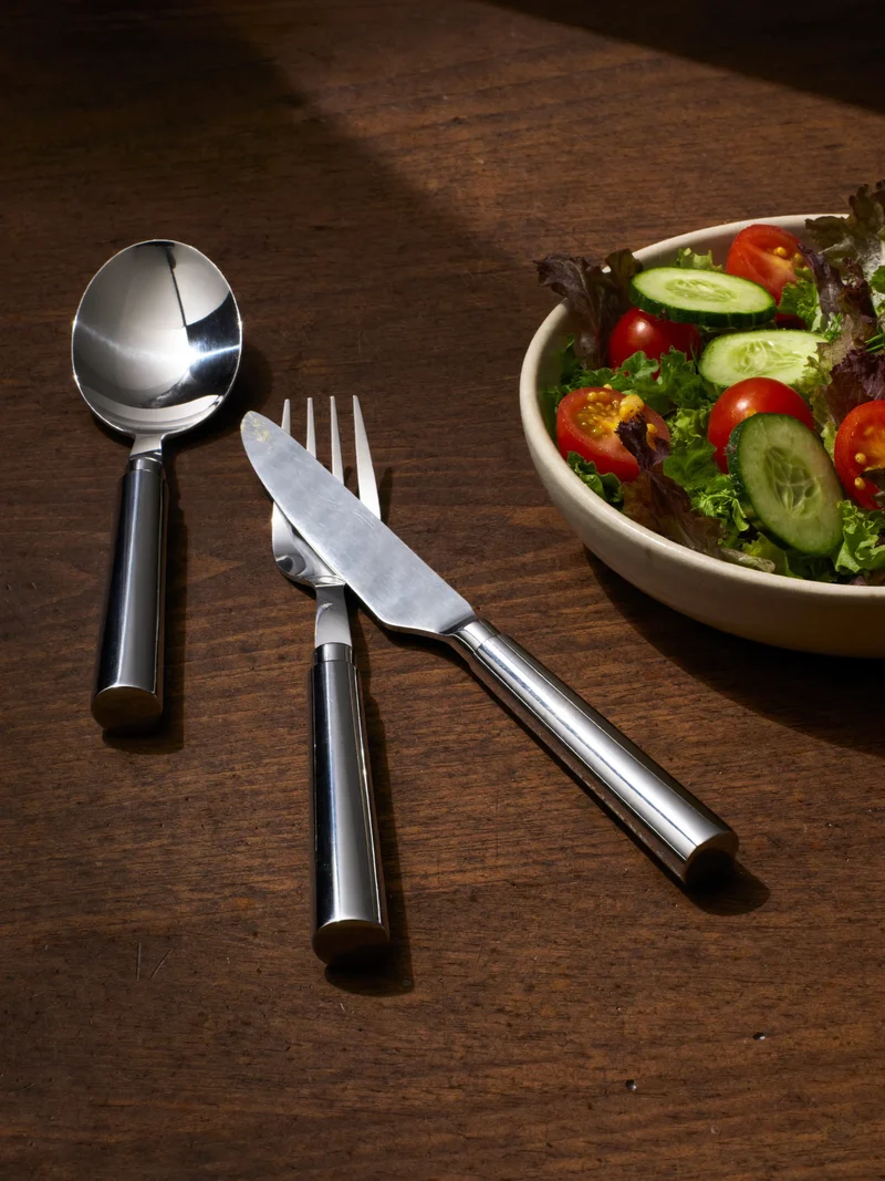 Serveringsske, salatsalg og kagespade på et rustikt træbord ved en skål salat